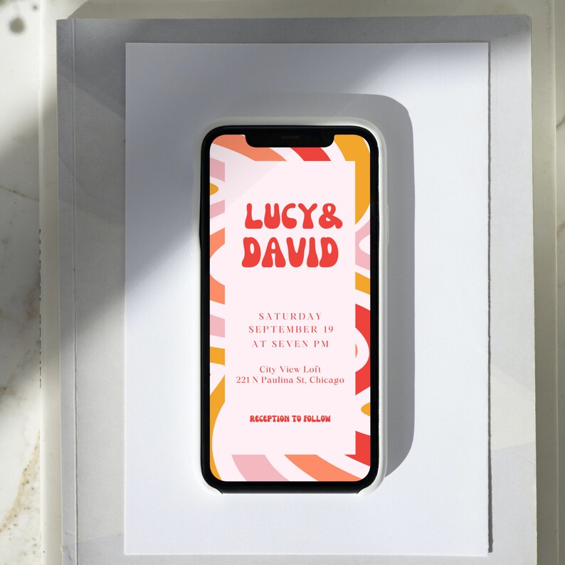 May include: A mobile phone screen displaying a wedding invitation with a colorful abstract background. The invitation reads "Lucy & David" in a red, bubbly font. The text below reads "Saturday, September 19 at Seven PM, City View Loft, 221 N Paulina St, Chicago, Reception to Follow."