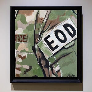 May include: Square framed painting of a military uniform. The painting features a camouflage pattern with the word "FORCE" visible on a patch. A white patch with "EOD" in bold black letters is also present.