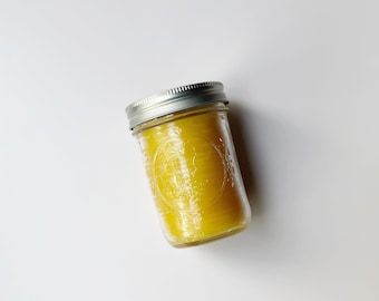 May include: A glass jar with a silver lid filled with a yellow substance. The jar has a textured surface.