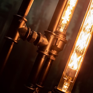 K&ouml;nnte beinhalten: Nahaufnahme einer schwarzen Metallrohrlampe mit zwei Edison-Gl&uuml;hbirnen. Die Rohre sind mit Armaturen verbunden und die Gl&uuml;hbirnen sind freiliegend.