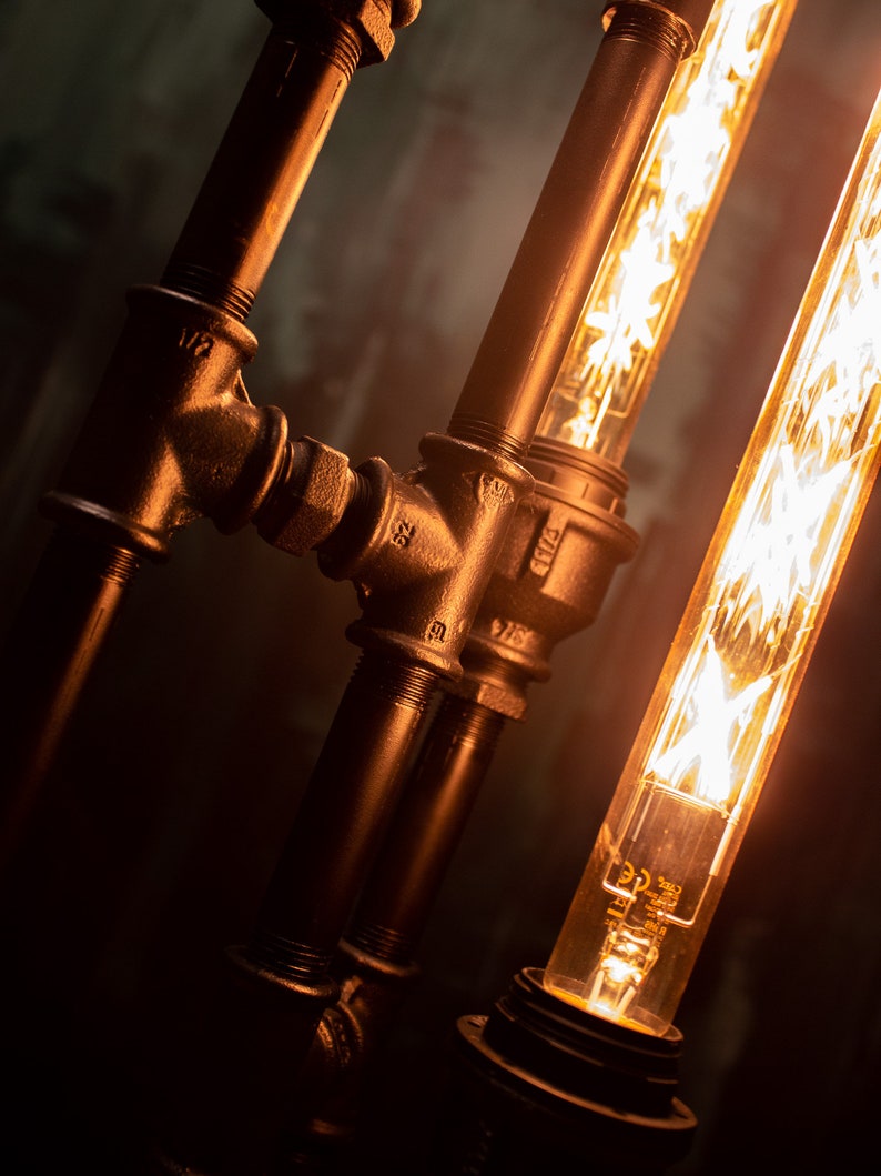 K&ouml;nnte beinhalten: Nahaufnahme einer schwarzen Metallrohrlampe mit zwei Edison-Gl&uuml;hbirnen. Die Rohre sind mit Armaturen verbunden und die Gl&uuml;hbirnen sind freiliegend.