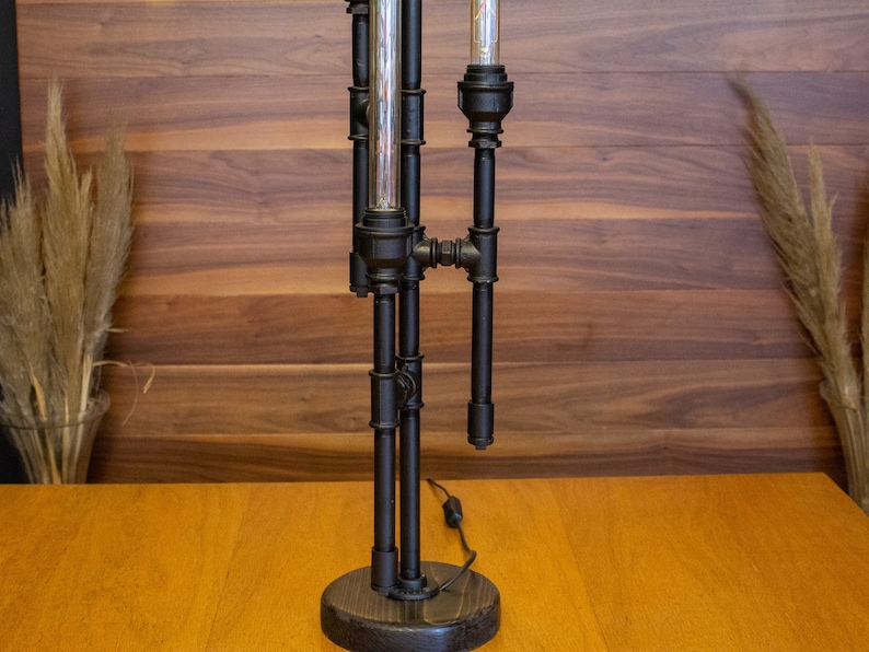 K&ouml;nnte beinhalten: Eine schwarze Tischlampe aus Metall mit einem einzigartigen Industriedesign. Die Lampe hat drei Gl&uuml;hbirnen und ein schwarzes Kabel.