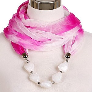 May include: A pink and white ombre scarf with a white beaded necklace attached. The scarf is made of a sheer fabric and the beads are large and oval shaped.