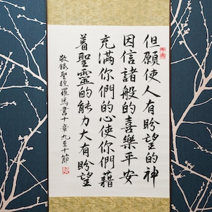 May include: An Asian scroll featuring black calligraphy on white paper, framed by a gold and cream border. It hangs against a dark blue backdrop with a white floral design. The text is in Chinese, and the scroll is a traditional art piece.