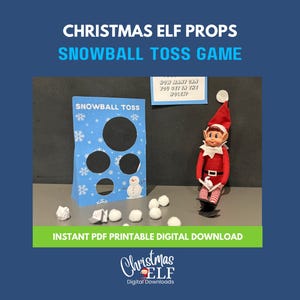 May include: A Christmas Elf Snowball Toss Game set. The game features a blue target with snowflake and snowman designs, and a red and white elf figurine. The target has the text "Snowball Toss". White paper snowballs are scattered on the surface.