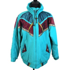 May include: A teal and burgundy vintage ski jacket with a hood. The jacket features a color block design with gold and teal accents. It has a zipper closure and two front pockets. The jacket is displayed on a mannequin.