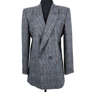 May include: A gray double-breasted blazer with a plaid pattern. The blazer has a notched lapel, two front pockets, and two buttons. The fabric has a mix of gray, red, and brown threads.