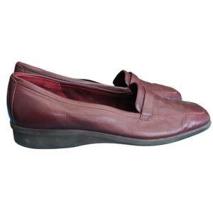 May include: A pair of burgundy leather loafers. The shoes have a classic slip-on design with a rounded toe and a low heel. The leather appears smooth and has a slight sheen. The interior lining is a darker shade of red.