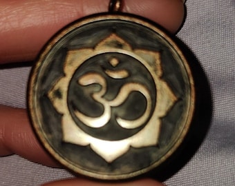 May include: A round, dark brown pendant with a silver Om symbol inside a flower design.