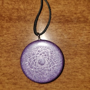 May include: A purple round pendant with a white mandala design hangs from a black cord.