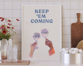 Peut inclure: Une impression encadrée blanche avec le texte "KEEP 'EM COMING" en lettres bleues. Deux mains tiennent des verres à vin avec un dégradé bleu et violet. L'impression est accrochée à un mur carrelé blanc au-dessus d'un comptoir avec un vase de fleurs rouges, une planche à découper en bois, un bol de boules blanches et un bol rose.