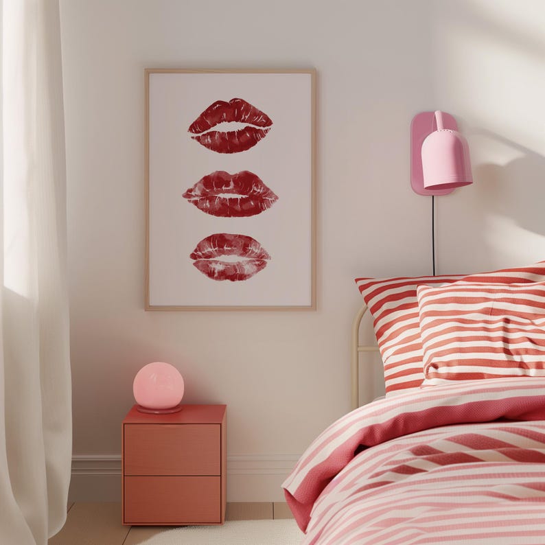 Puede incluir: Una impresi&oacute;n enmarcada con tres marcas de besos de l&aacute;piz labial rojo sobre un fondo blanco. La impresi&oacute;n est&aacute; colgada en una pared blanca sobre una mesita de noche roja con una l&aacute;mpara rosa. Una cama con ropa de cama a rayas rojas y blancas est&aacute; en el fondo.