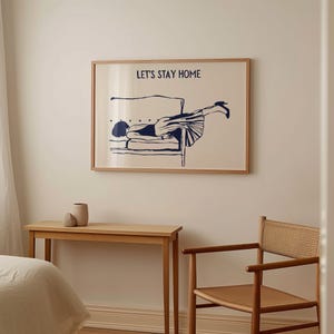 May include: A framed print with a blue illustration of a person lying on a couch. The text "Let's Stay Home" is printed above the illustration.