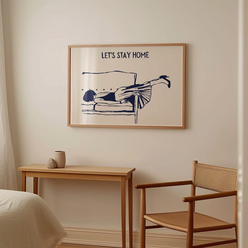 May include: A framed print with a blue illustration of a person lying on a couch. The text "Let's Stay Home" is printed above the illustration.