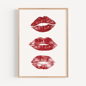 Puede incluir: Tres huellas de l&aacute;piz labial rojo en una fila sobre un fondo blanco, enmarcadas en un marco de madera claro.