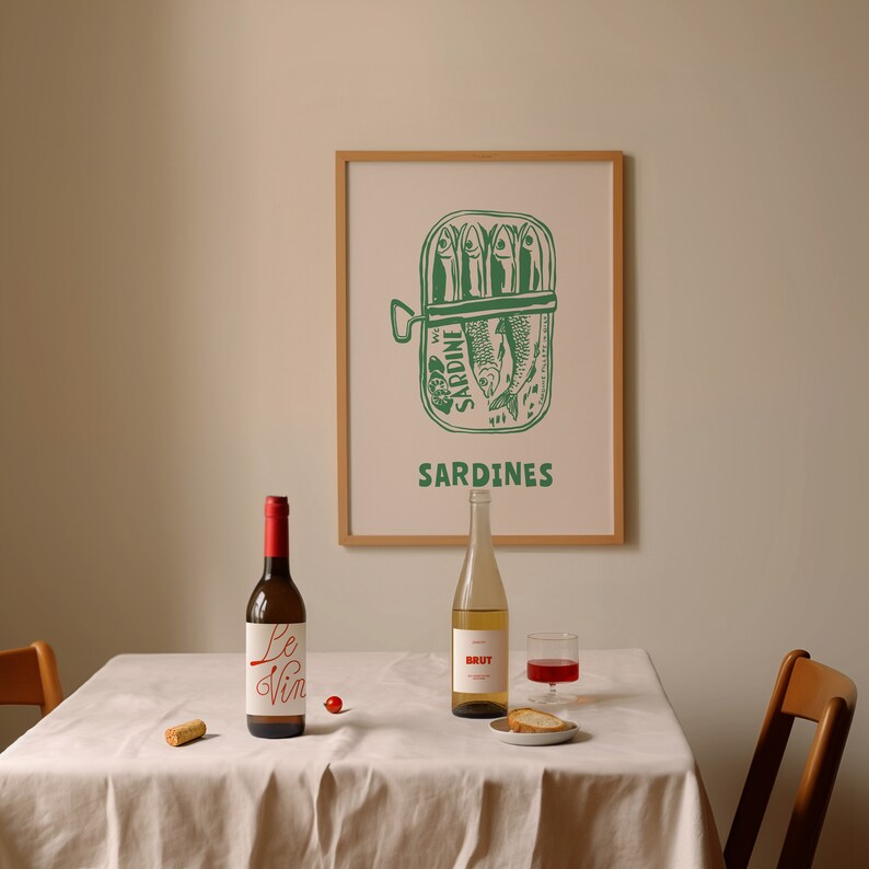 May include: A white tablecloth with a bottle of wine labeled "Le Vin" and a bottle of sparkling wine labeled "BRUT" on a table with a framed print of a sardine can with the text "SARDINES".