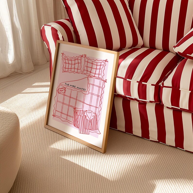 Puede incluir: Una ilustraci&oacute;n enmarcada de una cama rosa y blanca con una camisa a rayas rojas y blancas en la parte superior. El texto "Five more minutes" est&aacute; escrito en rojo en la cama. El marco est&aacute; sentado en un sof&aacute; a rayas blancas y rojas.