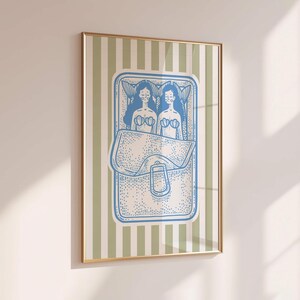 Pu&ograve; includere: Una stampa artistica incorniciata con un'illustrazione blu e bianca di due sirene all'interno di un contenitore a forma di borsa. Lo sfondo presenta strisce verticali in verde chiaro e bianco. La cornice &egrave; dorata.