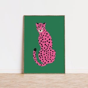 May include: A framed art print featuring a stylized pink cheetah with black spots, set against a vibrant green background. The cheetah is depicted in a seated pose, with a focused expression. The artwork is displayed in a wooden frame.