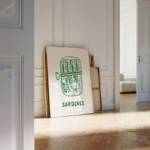 May include: A white framed poster with a green illustration of a can of sardines. The can has the words "WC Sardine" and "Sardines" printed on it.