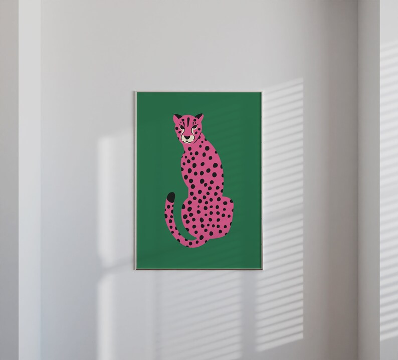 May include: A framed art print featuring a pink cheetah with black spots, set against a vibrant green background. The cheetah is depicted in a seated pose, with its tail curled. The artwork is displayed on a white wall, adding a pop of color to the space.