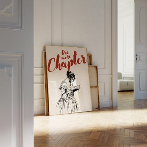 May include: A framed print with a black and white illustration of a woman reading a book. The text "One more Chapter" is written in red cursive letters.