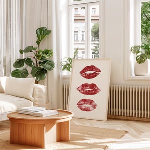 Puede incluir: Una impresi&oacute;n enmarcada en blanco con tres marcas de besos de l&aacute;piz labial rojo dispuestas verticalmente. La impresi&oacute;n est&aacute; colgada en una pared blanca en un sal&oacute;n.