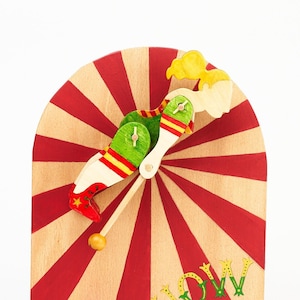 May include: A wooden toy with a red and white striped background. A painted figure of a person in a green and red outfit is attached to a spinning arm. The words "Show Time" are painted in green and yellow letters on the background.