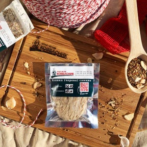 May include: A package of sausage casing labeled "Kovbasnyk" sits on a wooden cutting board with garlic cloves and spices. A wooden spoon filled with spices and a red mesh bag are also visible. The text "Scan me" is on the package.