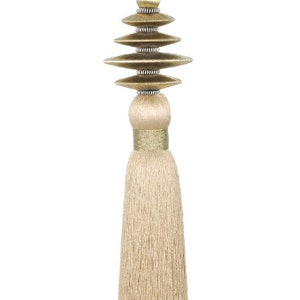 Peut inclure: Un pompon beige avec un motif géométrique doré. Le pompon est fait d'un matériau doux et soyeux et a une longue frange fluide.