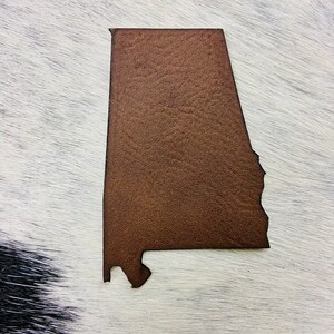 May include: A brown leather cutout of the state of Alabama.