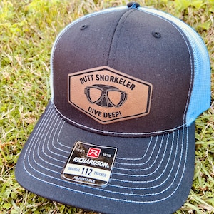 May include: Black and blue trucker hat with a brown leather patch that says "Butt Snorkeler Dive Deep!" and a Richardson 112 label.