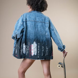 K&ouml;nnte beinhalten: Eine blaue Jeansjacke mit verblasstem schwarzem Design auf dem unteren R&uuml;cken, mit wei&szlig;em und rotem Text. Die Jacke wird mit schwarzen Stiefeln und einem Skateboard getragen. Der Text enth&auml;lt S&auml;tze wie "LOVE LIVE LIFE" und "LIFE IS WHAT YOU MAKE IT."