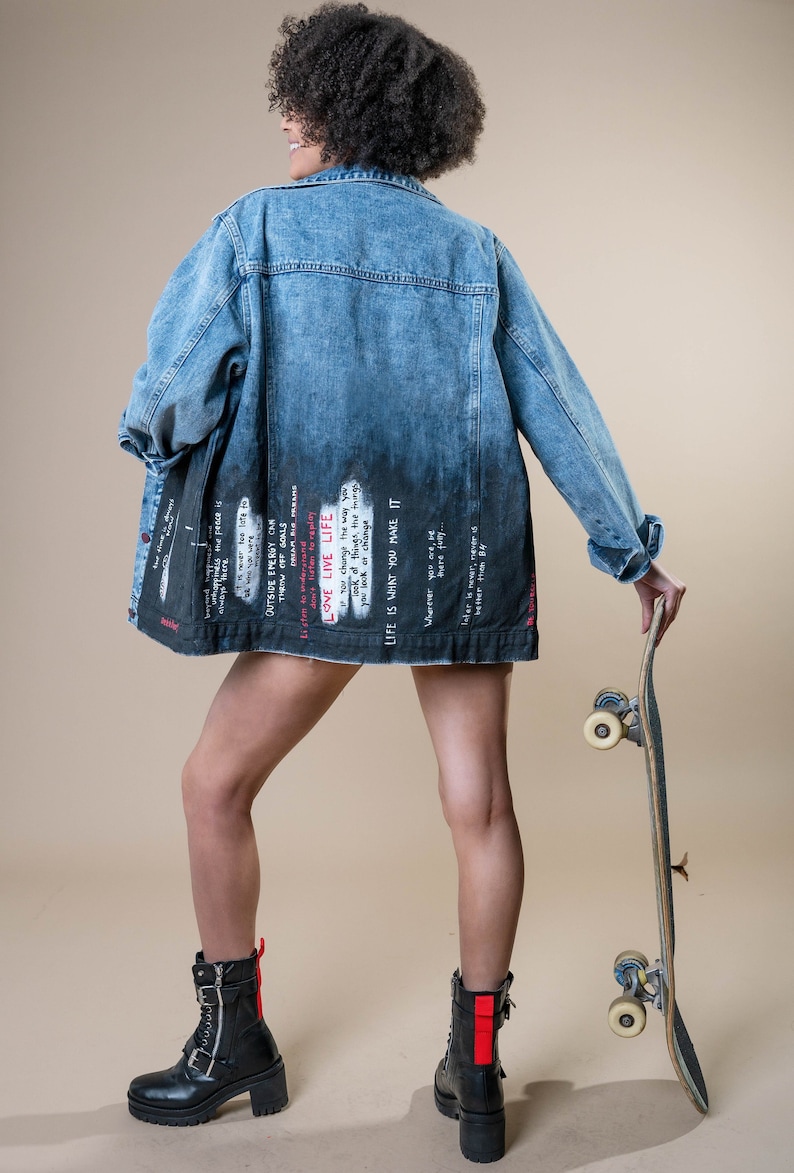 K&ouml;nnte beinhalten: Eine blaue Jeansjacke mit verblasstem schwarzem Design auf dem unteren R&uuml;cken, mit wei&szlig;em und rotem Text. Die Jacke wird mit schwarzen Stiefeln und einem Skateboard getragen. Der Text enth&auml;lt S&auml;tze wie "LOVE LIVE LIFE" und "LIFE IS WHAT YOU MAKE IT."