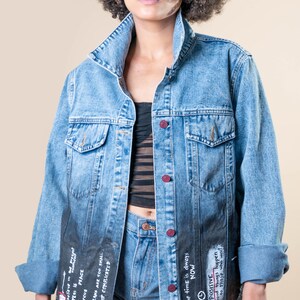 K&ouml;nnte beinhalten: Hellblaue Jeansjacke mit verblasstem schwarzem Unterteil, handschriftlichem Text und roten Kn&ouml;pfen. Die Jacke wird mit Jeansshorts kombiniert. Der Text enth&auml;lt S&auml;tze wie "Stay Positive" und "The time is always NOW."