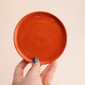 Może przedstawiać: Jasno pomarańczowy ceramiczny spodek, idealny do wyeksponowania małych przedmiotów lub jako element dekoracyjny.