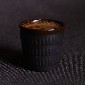 May include: A close-up of a dark brown ceramic coffee cup filled with coffee. The cup has a textured, ridged design.
