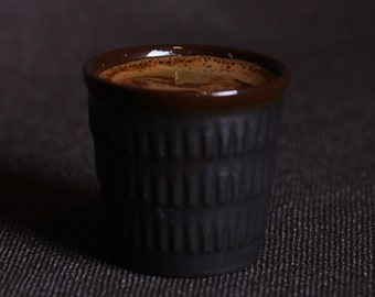 Può includere: Primo piano di una tazza da caffè in ceramica marrone scuro piena di caffè. La tazza ha un design testurizzato e rigato.