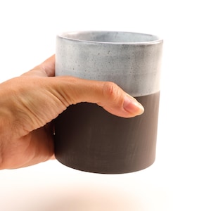 May include: A ceramic mug with a white top and a dark grey bottom. The mug is speckled with white flecks.