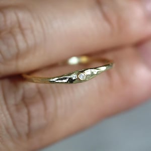 Puede incluir: Un anillo de oro con superficie texturizada y dos pequeños diamantes. El anillo tiene una forma orgánica y un acabado pulido. Los diamantes están engastados en un diseño minimalista. Ideal para el uso diario.