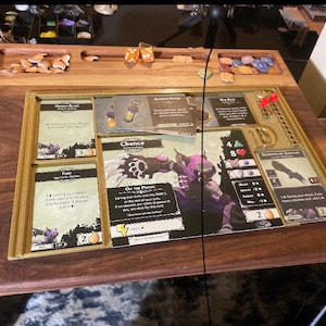May include: A wooden game board with a gold trim and compartments for cards and dice. The board has a dark wood finish and is designed for a tabletop game. The board is set up for a game with cards and dice.