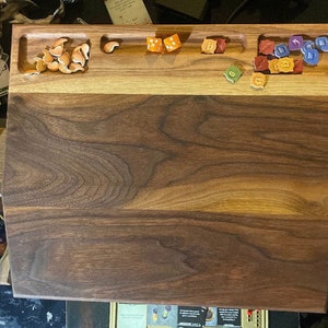 May include: A wooden game board with a light brown top and a dark brown bottom. The board has several compartments for dice and other game pieces. There are several dice and game pieces on the board, including orange, red, blue, and green dice.