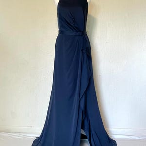 May include: A navy blue formal gown with a halter neckline and a flowing skirt. The dress features a fitted bodice, a waist sash, and a ruffled overlay on the skirt. The dress is displayed on a mannequin.