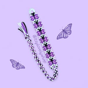 May include: Two handmade friendship bracelets in shades of purple, black, and white. One bracelet features a woven pattern, while the other is braided. The background is a light purple with two butterfly illustrations and the text "@itzylovelyshop".