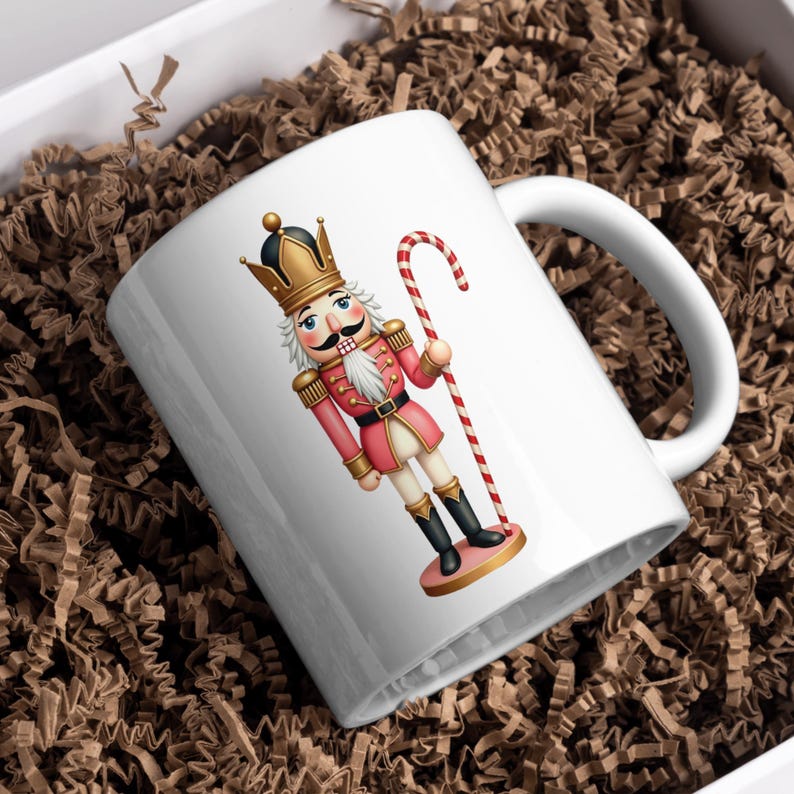 Może przedstawiać: Biały ceramiczny kubek z kolorową ilustracją żołnierza dziadka do orzech&oacute;w w r&oacute;żowym mundurze, złotej koronie i laseczce. Kubek znajduje się w białym pudełku z brązowym wypełniaczem papierowym, idealny na świąteczne prezenty.