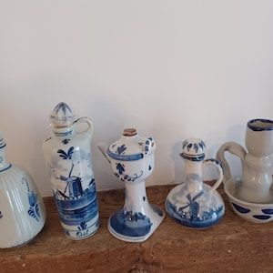 May include: A collection of blue and white ceramic decorative items, including bottles and a small oil lamp. The items are arranged on a wooden shelf. The bottles feature windmill and floral designs.