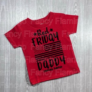 May include: Red t-shirt with a black graphic that says "Good Friday til my baby comes home" with an American flag design.