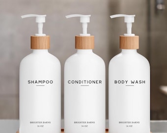 May include: Three white pump bottles with bamboo lids and labels reading "Shampoo", "Conditioner", and "Body Wash". Each bottle contains 16 ounces of product and is labeled "Brighter Barns". The bottles are displayed on a wooden tray.