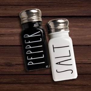 Puede incluir: Salero y pimentero negros y blancos con tapas plateadas. Los shakers est&aacute;n etiquetados con "SALT" y "PEPPER" en una fuente simple y moderna.