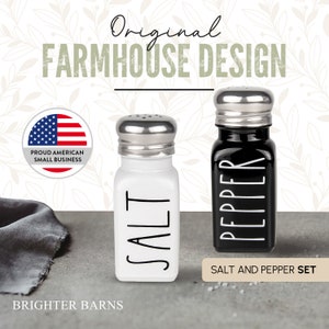Puede incluir: Juego de salero y pimentero con cuerpos de cer&aacute;mica blanca y negra y tapas plateadas. Los shakers tienen las palabras "SALT" y "PEPPER" impresas en negro. El juego est&aacute; etiquetado como "SALT AND PEPPER SET".